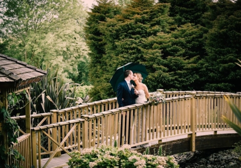 Couple embracing on a wooden bridge with lush greenery at Fernhill House Hotel.