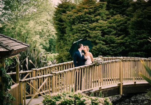 Couple sharing an umbrella on a garden bridge at Fernhill House Hotel.