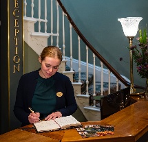Receptionist warmly greets guests at Fernhill House Hotel reception desk.