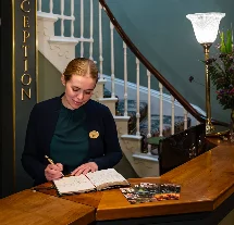 Hotel receptionist welcomes guests in elegant lobby with ornate chandelier.