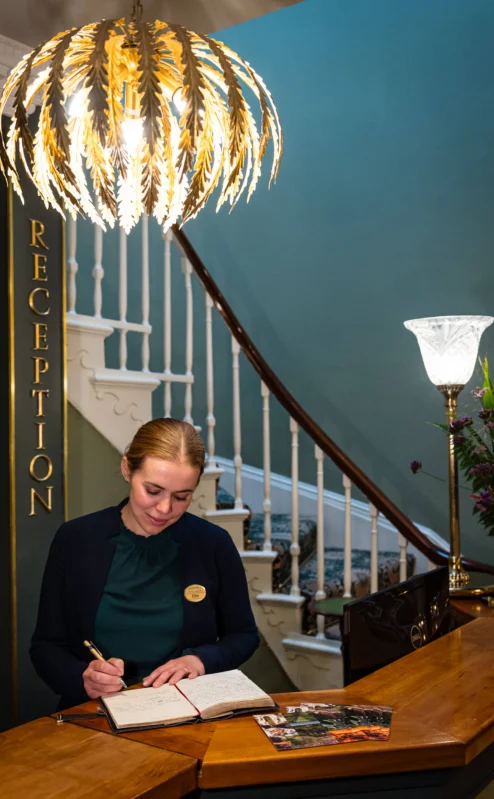 Hotel receptionist welcomes guests in elegant lobby with ornate chandelier.