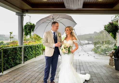 A happy couple under an umbrella at Fernhill House Hotel's scenic entrance.