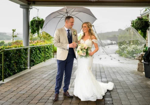 A couple in wedding attire under an umbrella at Fernhill House Hotel.