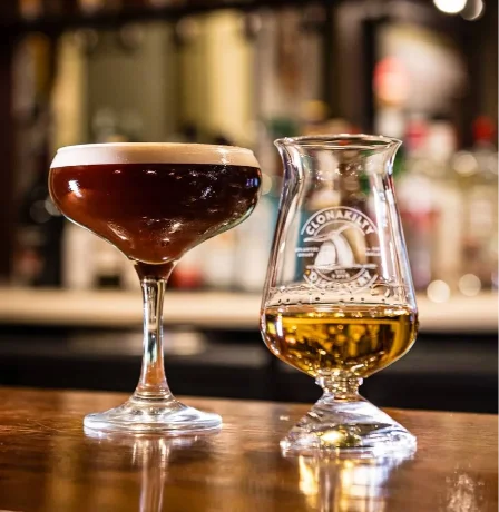 A cosy bar setting with a cocktail and whisky glass on a wooden counter.