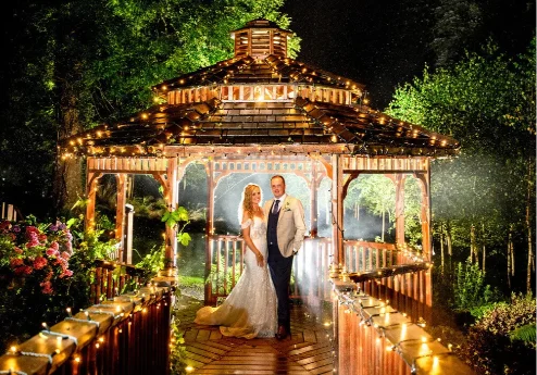 A couple poses by a lit gazebo in a lush garden at night.