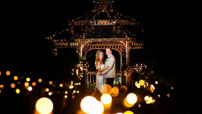 Couple embraces under fairy-lit gazebo at Fernhill House Hotel garden.