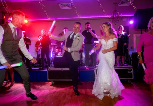 A joyous couple dancing at a lively wedding reception with friends under vibrant lights.