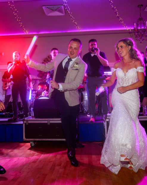 A couple dances joyfully at Fernhill House Hotel wedding reception, surrounded by family and colourful lights.