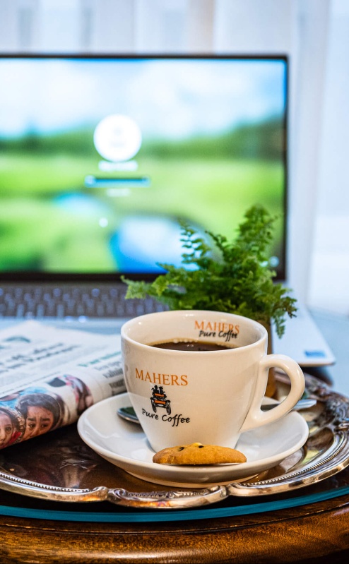 Cosy hotel room with tea, biscuit, and newspaper on a table beside a laptop.