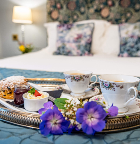 A cosy hotel room with tea and scones on a tray, set on a comfortable bed.
