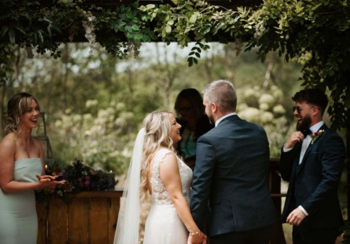 A couple exchanges vows in a lush garden setting with family under a leafy arch at Fernhill House Hotel.