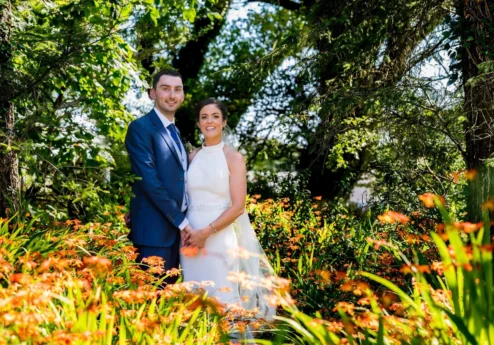 A couple smiling among vibrant flowers in a sunny garden at Fernhill House Hotel.