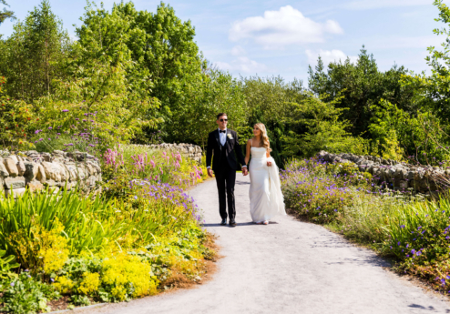 Couple walking hand in hand through a lush garden path in Fernhill House Hotel grounds.