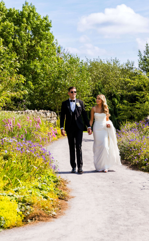 Couple walking hand in hand through a lush garden path in Fernhill House Hotel grounds.