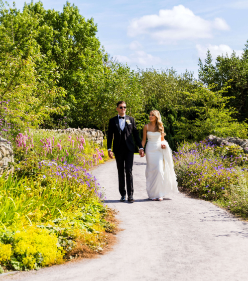 Couple walking hand in hand through a lush garden path in Fernhill House Hotel grounds.