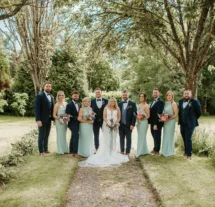A wedding group stands under trees in Fernhill House Hotel’s lush garden.