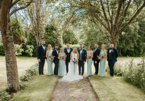 A wedding group stands under trees in Fernhill House Hotel’s lush garden.