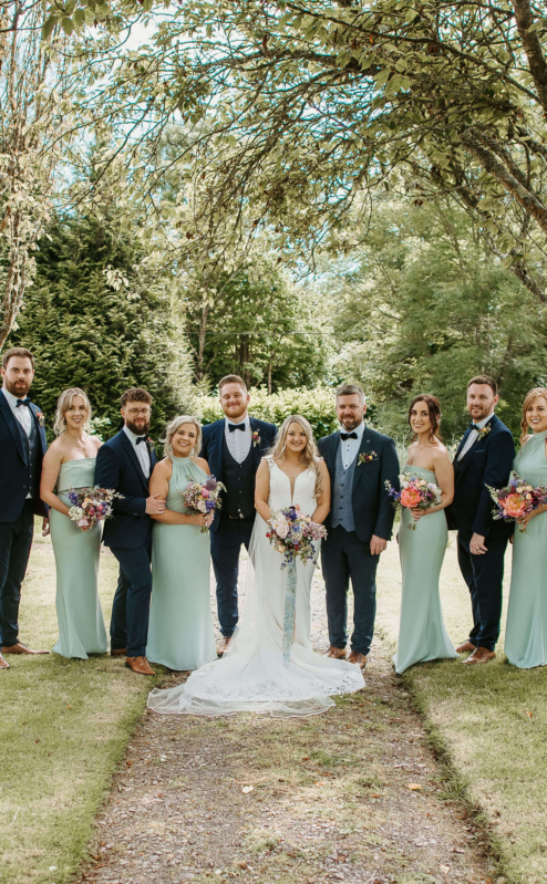 A wedding party smiling under trees in Fernhill House Hotel's lush garden.