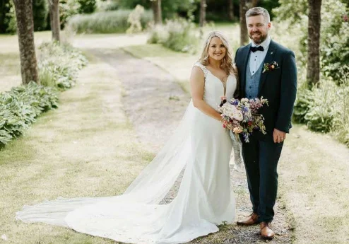 Couple in wedding attire smiling in a lush garden at Fernhill House Hotel.