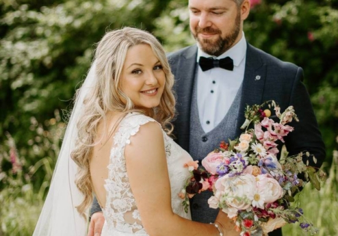 A couple in wedding attire share a joyful moment in lush garden at Fernhill House Hotel.
