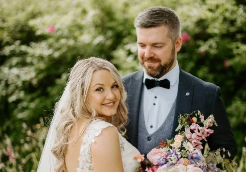 A happy couple in wedding attire smiling in a lush garden.