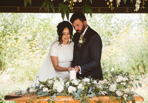 A couple lights a unity candle under a floral gazebo at Fernhill House Hotel garden.