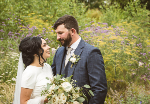 A couple smiling in a garden at Fernhill House Hotel, surrounded by vibrant wildflowers.