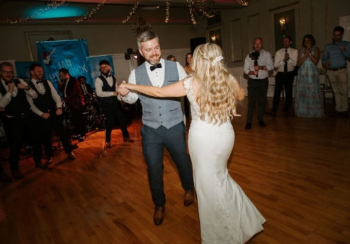 A couple dancing joyfully at a wedding reception in a warmly lit hotel ballroom.