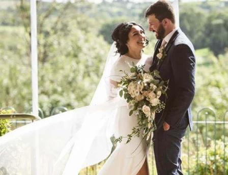 A joyful couple in wedding attire share a moment on a lush garden terrace at Fernhill House Hotel.
