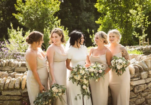 Group of smiling women in elegant dresses holding bouquets at Fernhill House Hotel garden.