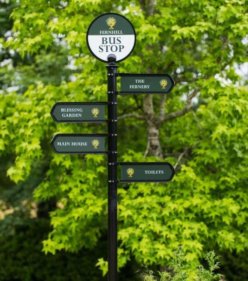 Signpost in lush Fernhill House Hotel garden with directions to amenities.