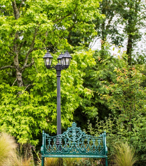 Lush garden with ornate bench and directional signs at Fernhill House Hotel.