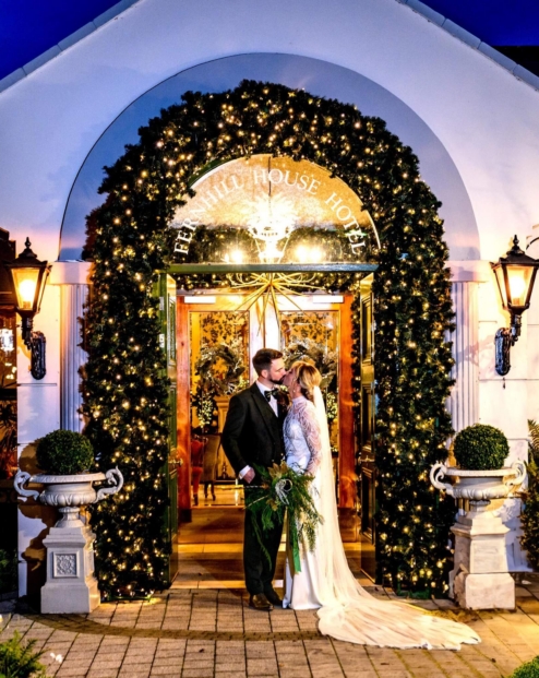 A couple embraces under festive lights at Fernhill House Hotel's entrance.