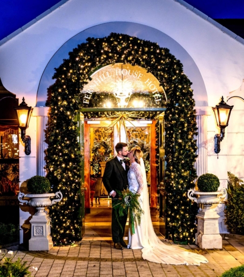 A couple embraces under festive lights at Fernhill House Hotel's entrance.