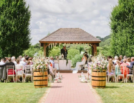 Couple exchanging vows in a picturesque garden with family gathered.