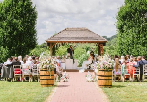 Couple exchanging vows in a picturesque garden with family gathered.