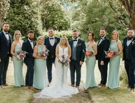 A wedding party poses in a lush garden at Fernhill House Hotel.