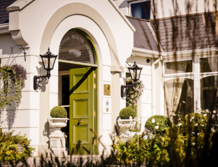 Warm entrance of Fernhill House Hotel with open green door and welcoming floral decor.