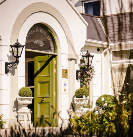 Warm entrance of Fernhill House Hotel with open green door and welcoming floral decor.