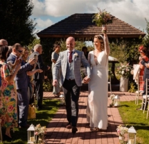 A joyous couple walks down an outdoor aisle, surrounded by smiling guests at Fernhill House Hotel.
