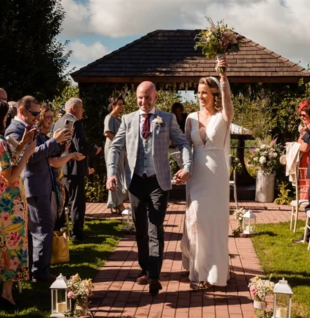 A joyful couple walk hand in hand down an outdoor aisle, surrounded by celebrating family and friends at Fernhill House Hotel.