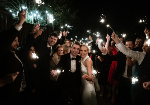 A joyous couple surrounded by loved ones holding sparklers at night outdoors.
