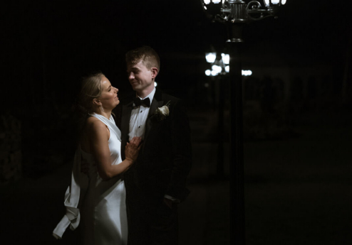 A couple, elegantly dressed, share a warm moment under lamplight at Fernhill House Hotel at night.
