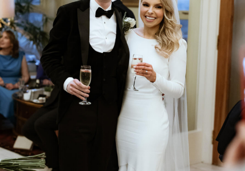 A smiling couple in formal attire holding glasses, standing in an elegant hotel setting.