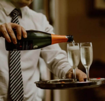 Server pouring champagne into glasses on a tray in a cosy hotel setting.