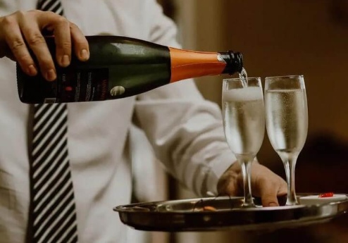 Server pouring champagne into glasses on a tray in a cosy hotel setting.