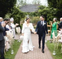 A joyful couple walks down an outdoor aisle at Fernhill House Hotel, surrounded by clapping family.