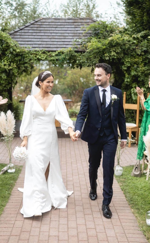 A joyful couple walks down an outdoor aisle at Fernhill House Hotel, surrounded by cheering family and friends.