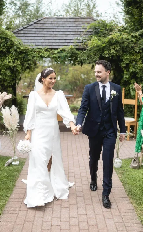 A joyful couple walks down an outdoor aisle at Fernhill House Hotel, surrounded by clapping family.