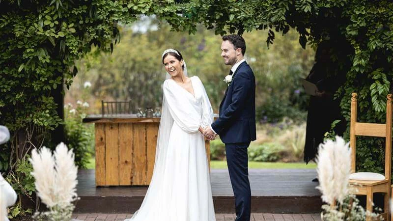 A couple joyfully stands in a lush garden at Fernhill House Hotel, exchanging vows.
